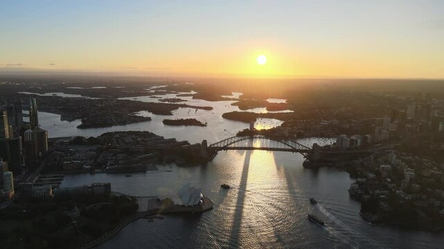 Cinematic drone video from above Sydney harbour giving an arial view of the opera house and harbour bridge with the sunset in the background