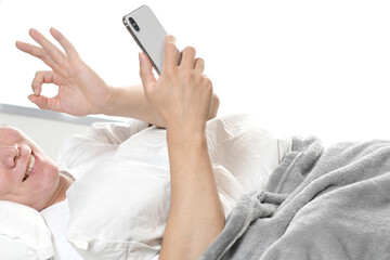 ベッドでスマホを持ちOKをする若い男性