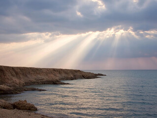Dramatic ocean coastline. Sun rays piercing through clouds over tranquil sea landscape