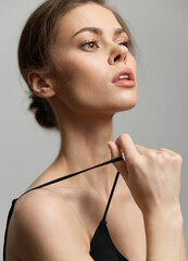 Pensive young woman in elegant black dress pulling shoulder strap, expressing confidence and poise....
