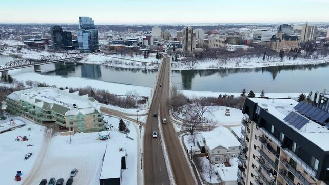 City street with a bridge over a river and a large building in the background. The sky is cloudy and the snow is falling