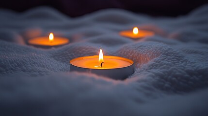 Three candles burning on soft white fabric, dark background, relaxation