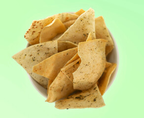 Seasoned pita chips in a white bowl on a soft green background. Perfect for snack or appetizer visuals.