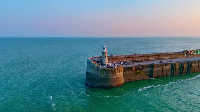 Lighthouse stand tall at golden hour skyline, aerial panning view