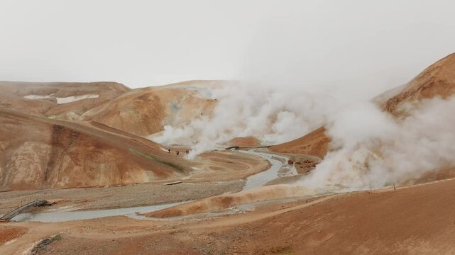 50fps aerial shot of Kerlingarfj&ouml;ll&rsquo;s geothermal area. Steam rises from vents amidst orange hills, with visitors exploring the rugged terrain. Ideal for nature, travel, and adventure projects.