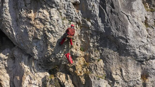 Aerial view of mountain rescuer abseiling on a rocky wall hanging on a rope