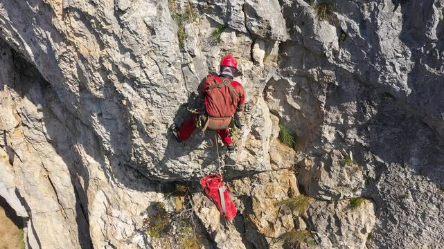 Aerial view of mountain rescuer abseiling on a rocky wall hanging on a rope