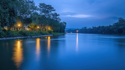 Fototapeta premium Serene river scene at twilight with reflections and soft lights along the bank.