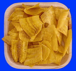 Crispy plantain chips in a wooden plate on a vibrant blue background. Perfect for snack or tropical...