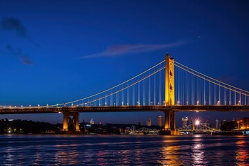 Fototapeta premium Night view of a suspension bridge over a river with city lights