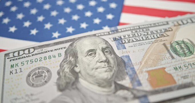 Strength of the dollar: The U.S. currency's role in global trade and finance. U.S. $100 bill featuring Benjamin Franklin against the backdrop of the American flag, relates to topics e.g. U.S. economy.