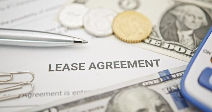 Property rental, leasing contracts, real estate, housing agreements, and property management. A close-up view of a lease agreement document with paperclips, coins, US dollar, and a pen placed on top.