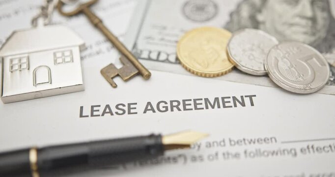Property rental, leasing contracts, real estate, housing agreements, and property management. A close-up view of a lease agreement document with a house key, coins, US dollar, and a pen placed on top.