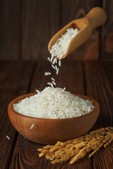 rice falling from scoop in bowl with ears near on wooden background