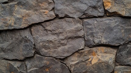 Obraz premium Textured stone wall featuring irregularly shaped dark rocks with hints of earthy tones, creating a rustic and natural appearance.