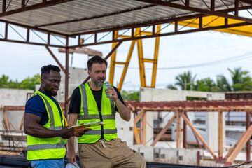 Two male engineers from different cultures and ages work together in a floor making factory. Senior supervisor discusses with his African engineer checking the concrete wall production system