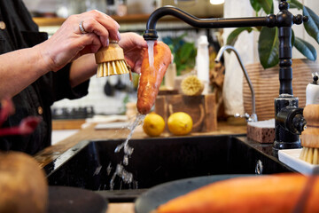 a woman in the kitchen washing vegetables and carrot  with a wooden brush, in a modern black sink