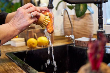 a woman in the kitchen washing vegetables and carrot  with a wooden brush, in a modern black sink