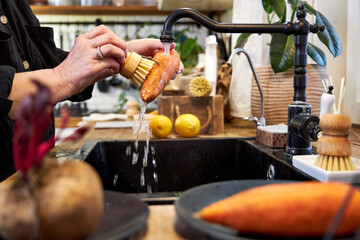 a woman in the kitchen washing vegetables and carrot  with a wooden brush, in a modern black sink