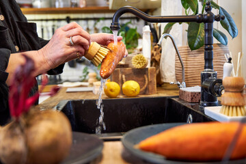 a woman in the kitchen washing vegetables and carrot  with a wooden brush, in a modern black sink