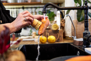 a woman in the kitchen washing vegetables and carrot  with a wooden brush, in a modern black sink