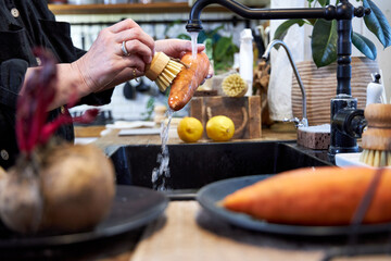 a woman in the kitchen washing vegetables and carrot  with a wooden brush, in a modern black sink