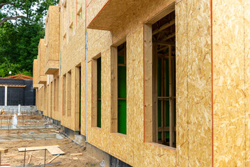 Close-up of a construction site featuring wooden framed buildings with OSB sheathing, representing...