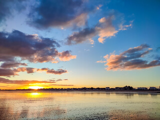 Vibrant colors fill the sky as the sun sets behind a coastal town, casting reflections on the...