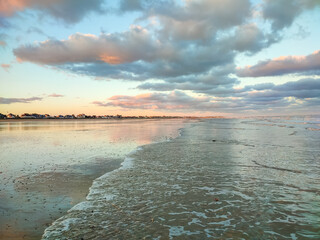 Gentle waves roll onto the sandy beach as colorful clouds reflect the warm sunset hues over the ocean