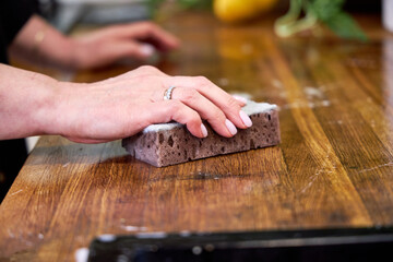 a woman sponges a wooden countertop in the kitchen, close-up of her hands