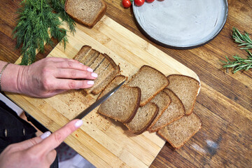 a woman slices rye gray bread on a wooden countertop in the kitchen