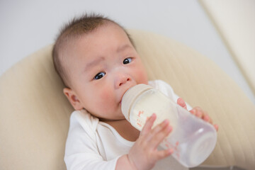 Adorable baby enjoying fresh milk bottle indoors