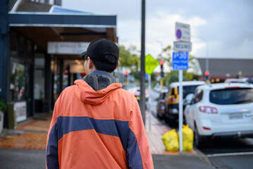 Man in orange raincoat walking on the pedestrian walkway of a busy city street. Auckland.
