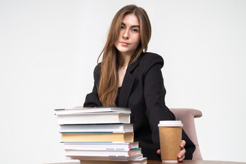 Pretty young girl in jacket sitting on a chair with stack of books on white background