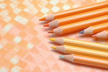 Obraz premium collection of pastel orange color pencils arranged on plaid pattern background, showcasing variety of soft hues