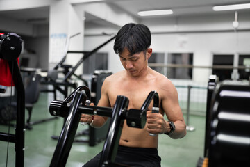 Healthy lifestyle, exercising and Asia people concepts. Muscular man doing shoulder and back presses on  shoulder and back machine in the gym	