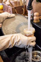 woman in white gloves washing a plate with a wooden brush, eco-friendly cleaning close-up of hands