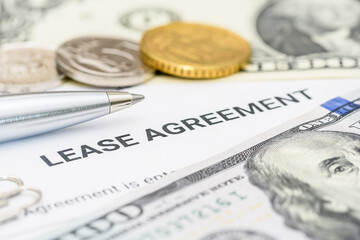 Property rental, leasing contracts, real estate, housing agreements, and property management. A close-up view of a lease agreement document with paperclips, coins, US dollar, and a pen placed on top.