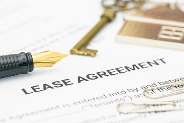 Property rental, leasing contracts, real estate, housing agreements, and property management. A close-up view of a lease agreement document with paperclips, a house key, and a pen placed on top.