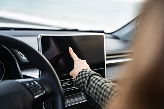 Side view of an unrecognizable woman using a GPS navigation system while driving her car. Female driver touching modern car dashboard. Screen multimedia system in automobile. Closeup.
