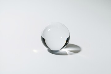 A clear glass sphere casts a shadow on a white background, showcasing its reflective properties.