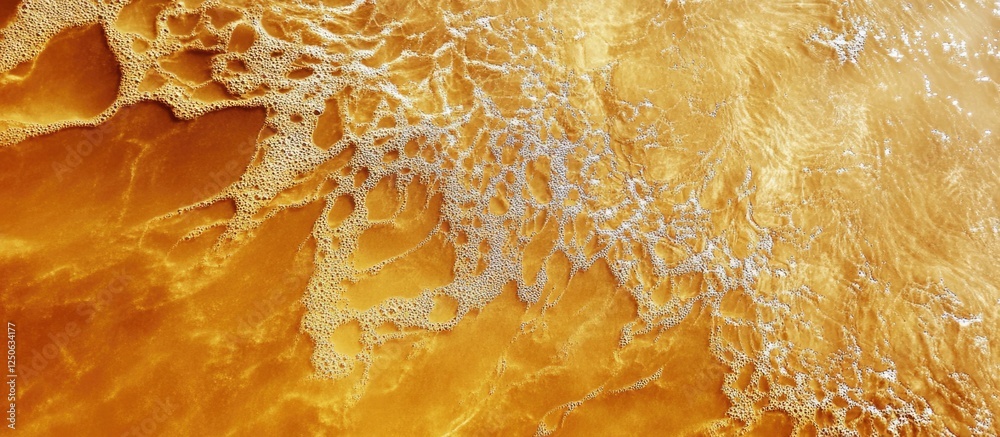 Aufkleber Golden sandy beach texture with waves creating a dynamic pattern in the sunlight ideal for background or nature themed projects.