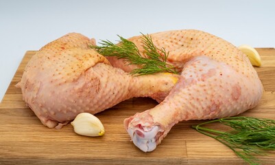 Fresh raw chicken legs with dill and garlic on a wooden board.