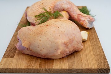 Fresh raw chicken legs with dill and garlic on a wooden board.