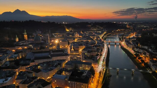 Sunset over Salzburg with illuminated buildings and river reflections. Aerial night view of Salzburg old town, red sunset sky at background, Austria