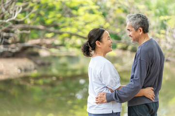 Obraz premium side view romantic asian senior couple standing in the nature park,embracing,looking each other,smile,concept of family,relationship,love,bonding