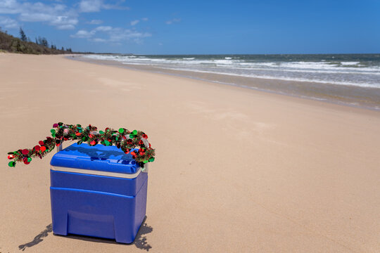 Christmas in Australia, blue esky cooler with tinsel decoration on beach, sand and ocean waves surf in background, festive season concept