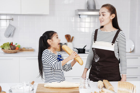 Smiling Asian mother teaching daughter child girl preparing and kneading the dough for baking homemade bakery baguette bread in kitchen together. Kid learning Homeschool Concept