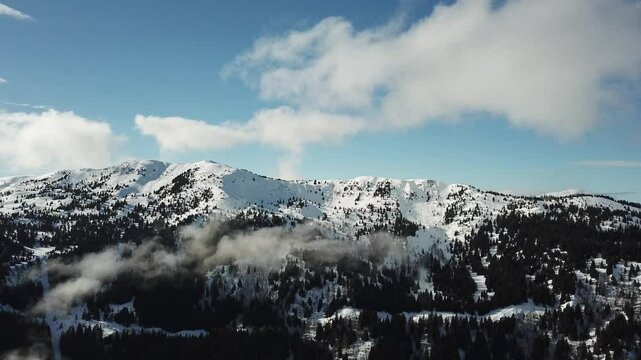 snow-covered mountain range, standing tall and majestic against the backdrop of a clear blue sky dotted with a few fluffy white clouds, in Alpes-Belledonne, France