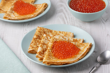 Savory crepes filled with fresh orange fish roe served on a light blue plate at a cozy breakfast table